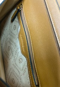 Vista interna di una borsa in pelle beige con fodera in tessuto beige stampata con "CAFENOIR" e una tasca con zip dotata di cerniera beige e tirazip in pelle.