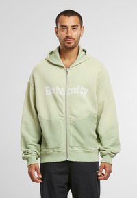 Hoodie zippé vert à coupe décontractée, avec deux poches avant, une section inférieure texturée et le logo "Reternity" en blanc.