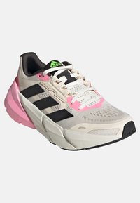 Sneaker légère avec une tige en mesh beige, des bandes noires, des accents roses et une semelle intercalaire texturée blanche avec une semelle extérieure en caoutchouc noire.