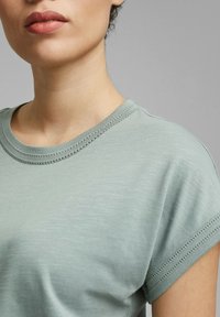 Gros plan d'une personne portant une chemise à manches courtes vert clair avec des coutures côtelées détaillées sur le col et les manches.