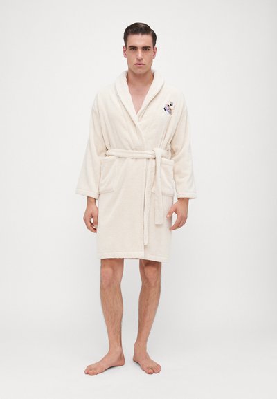 Bež bathrobe od frotira s šalom, teksturom od petlji, dizajnom za uvijanje, remenom i prednjim džepovima. Ima vezeni detalj.