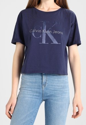 Granatowy krótki t-shirt bawełniany z okrągłym dekoltem, z jasnoszarym nadrukiem "Calvin Klein Jeans" i oversize'owymi rękawami.