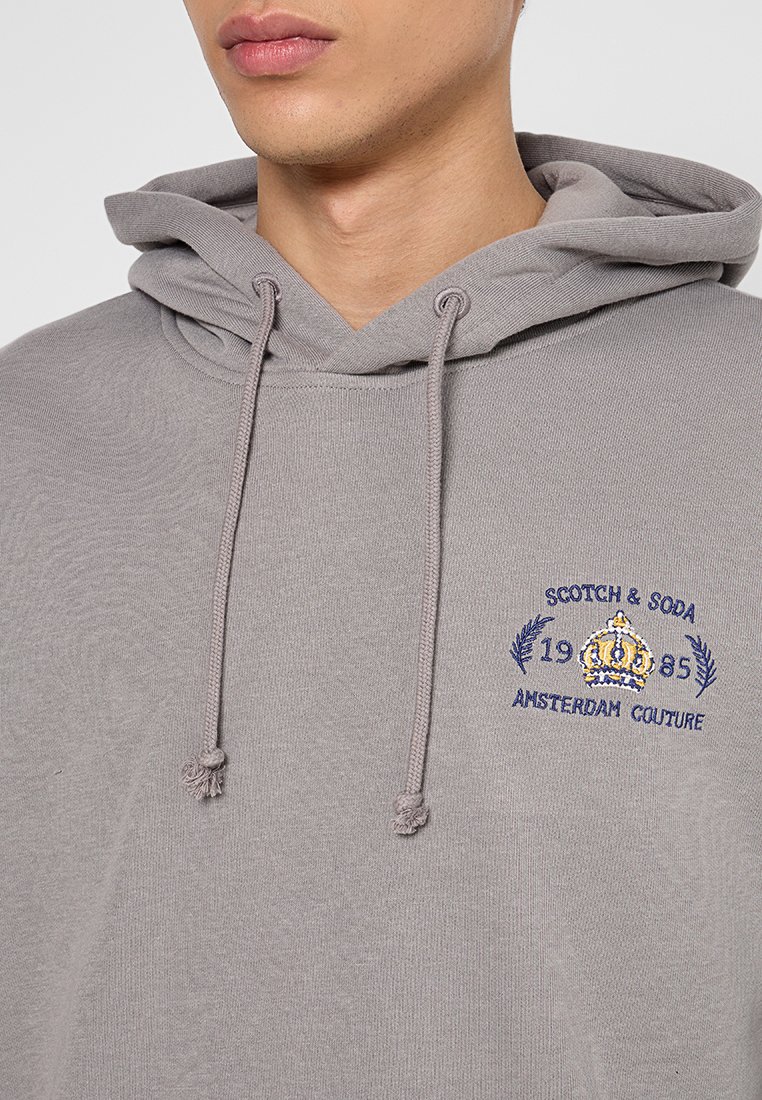 Grijze hoodie met een trekkoord, geborduurd logo met een kroon en tekstdetails, gemaakt van zacht materiaal met een comfortabele pasvorm.