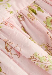Soft pink fabric with green and brown floral pattern and gathered, pleated texture.