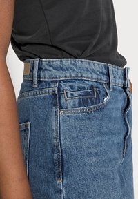 Jeans in denim blu a vita alta con taglio dritto, leggera scoloritura, dettagli di cucitura sottili e tasche posteriori.