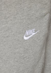 Nike logo on a light gray, textured fabric, with a prominent embroidered white swoosh. Material appears soft and casual.