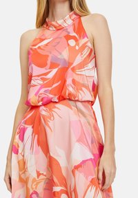Ärmlös halterklänning i orange och rosa blommönster, med en draperad livdel och flödande tyg som faller neråt.
