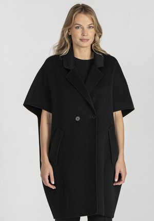 Czarna wełniana peleryna z kołnierzem z wycięciem, podwójnymi guzikami i bocznymi kieszeniami. Charakteryzuje się luźnym krojem i krótkimi rękawami.
