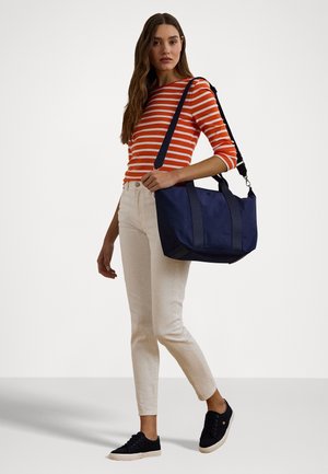 Sac fourre-tout navy avec des accents gris foncé, forme rectangulaire, double poignées et une bandoulière. Le modèle porte un haut rayé orange et un pantalon crème.