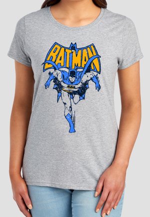 Woman wearing gray t-shirt with vintage-style blue and yellow Batman graphic showing Batman running forward.