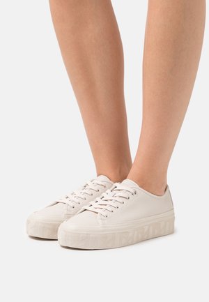 Białe niskie trampki, charakteryzujące się teksturowaną skórzaną cholewką, solidną gumową podeszwą i dekoracyjnym wzorem bieżnika. Sznurowadła są równomiernie zawiązane.