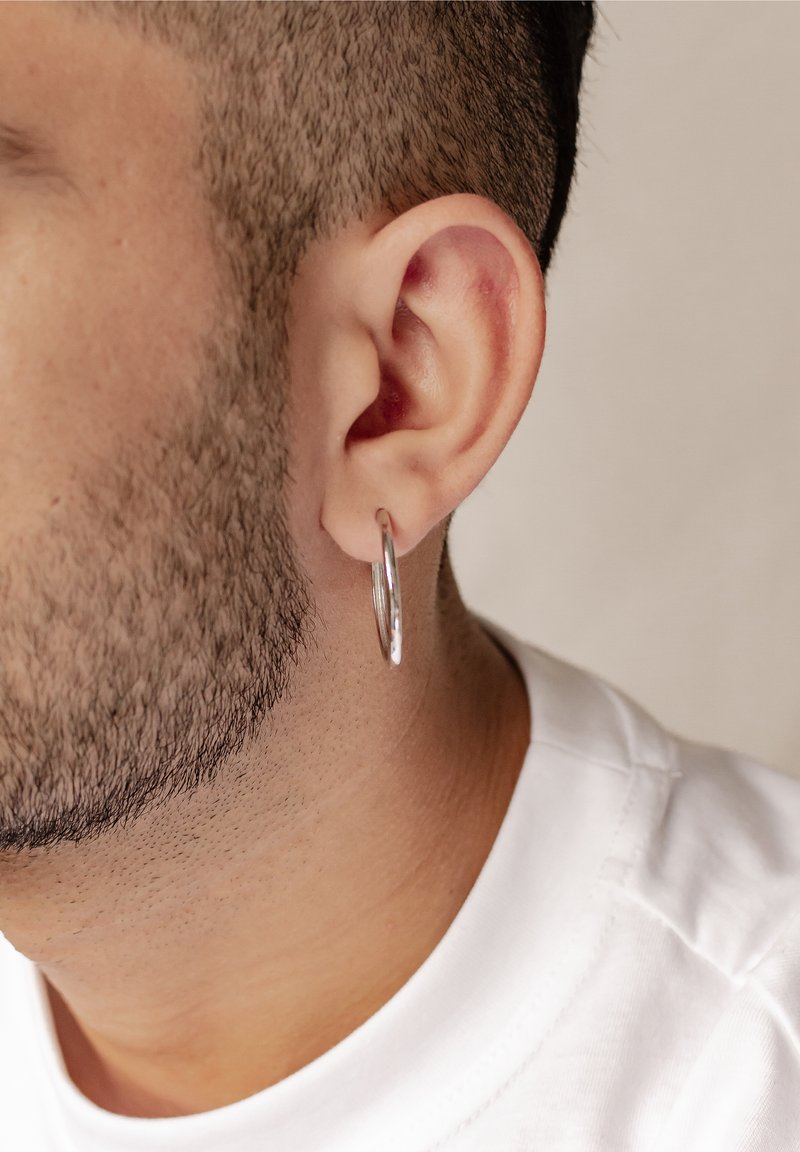 Boucle d'oreille en argent portée dans une oreille percée, présentant une surface lisse et polie ainsi qu'un design circulaire, sur une coupe de cheveux courte.