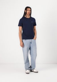 Mørkeblå bomulls t-skjorte med rund hals, kombinert med løse lyseblå jeans og svarte og hvite joggesko. Enkelt logo på skjorten.