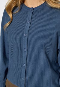 Blauwe geribbelde cardigan met een ronde hals en zeven knopen aan de voorkant. Zachte textuur, lange mouwen en een aansluitende pasvorm.