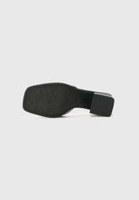 Suela de zapato de cuero negro con un tacón cuadrado. Presenta un patrón de agarre texturizado y costura visible a lo largo del borde.