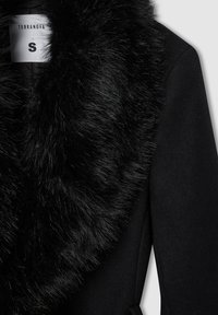 Cappotto nero con colletto in pelliccia sintetica, texture liscia e design su misura con spacco laterale. Etichetta visibile con "Terranova" e taglia "S".