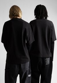 Divas cilvēkiem ir melnas kokvilnas t-kreklus ar īsām piedurknēm. Vienam no viņiem ir bikses ar izšuvumu un etiķeti sānu kabatā.