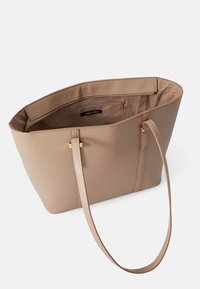 Sac fourre-tout beige en matériau structuré, avec un intérieur spacieux, des accents dorés, et une seule bandoulière pour le porter.