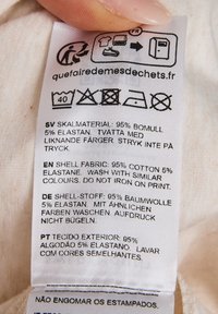 Verzorgingslabel met stofsamenstelling: 95% katoen, 5% elastaan. Bevat wasinstructies in meerdere talen en verzorgingsiconen.