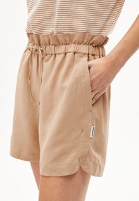 Beige linnen shorts met een elastische taille en trekkoord. Beschikt over zijzakken en een klein merklabel aan de zoom. Glad textuur.