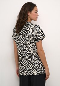 Zebra-patterned short-sleeve top in cream and black. Made from soft fabric, featuring a relaxed fit with a round neckline and back seam detail.