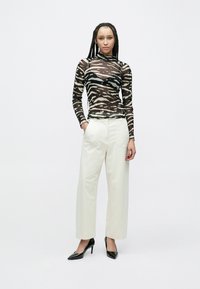 Μπλούζα με μακριά μανίκια και εφαρμοστή γραμμή από διάφανο υλικό με ασπρόμαυρο μοτίβο ζέβρας σε μαύρο και μπεζ, συνδυασμένη με λευκό παντελόνι φαρδιάς γραμμής και μαύρα τακούνια.