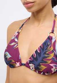 Μπικίνι τοπ σε μωβ χρώμα με τρίγωνα κύπελλα, με floral μοτίβο σε μπλε, ροζ και κίτρινο, με χρυσές λεπτομέρειες στα λουριά.