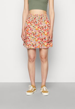 Saia com padrão floral e cintura elástica, apresentando flores multicoloridas sobre um fundo claro. Combinada com sapatos amarelos e uma blusa verde.