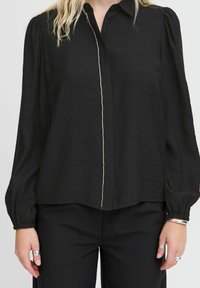 Black button-up blouse with long sleeves, featuring a textured fabric and a line of small silver accents along the center placket.