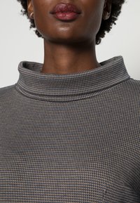 Zkrácený svetřík s vysokým límcem má texturovanou tkaninu v temně modro-bežovém kostkovaném vzoru, s měkkým, strukturovaným límcem.