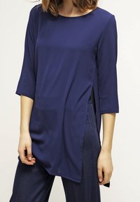 Marinblus, långärmad topp med rund halsringning, sidofickor och en mjuk textur, i kombination med mörka denimbyxor.