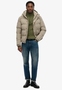 Beżowa pikowana kurtka z kapturem, zielony dziany sweter, niebieskie dżinsy i czarne botki za kostkę. Kurtka posiada zamek błyskawiczny i ściągacze przy mankietach.