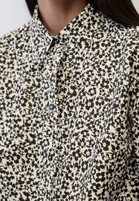 Camicia con bottoni caratterizzata da uno sfondo crema con un motivo floreale nero, colletto e chiusura con bottoni. Tessuto morbido con una superficie liscia.