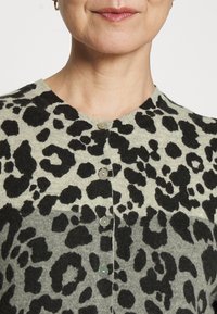 Il cardigan a maglia con stampa leopardata presenta uno sfondo grigio con macchie nere, un collo rotondo e cinque bottoni di chiusura sul davanti.