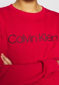 Czerwona bluza wykonana z miękkiego materiału, z okrągłym dekoltem, długimi rękawami oraz czarnym haftem z napisem "Calvin Klein" na przodzie.
