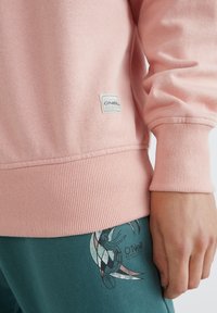 Lichtroze sweatshirt met geribbelde manchetten en zoom, voorzien van een logolabel. Gecombineerd met donkerteal broek met een grafische print.