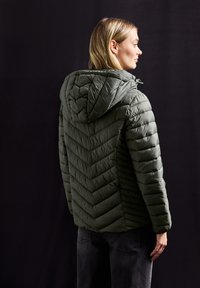 Olivgrön pufferjacka med en chevron-quiltad mönstring och huva. Har dragkedja och mjukt, strukturerat tyg.