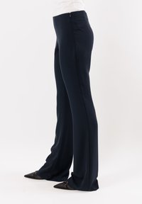 Pantaloni a gamba larga blu navy realizzati in un tessuto liscio, con una zip laterale discreta e dettagli di cucitura minimi. Abbinati a scarpe nere a punta.
