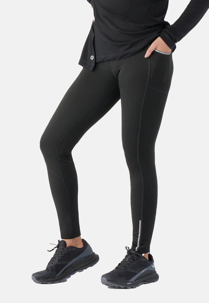 Zwarte leggings van een gladde, rekbare stof met zijzakken en reflecterende accenten. Combinatie met donkere sportschoenen voor een sportieve uitstraling.
