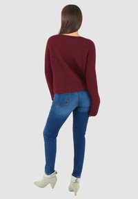 Maglione a maglia color bordeaux con scollo ampio, abbinato a jeans di denim blu e stivaletti chiari con tacco basso.