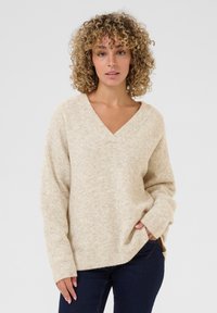 Beige V-hals sweater med en blød tekstur, s�ænkede skuldre og sideslidser. Har lange ærmer og en afslappet pasform.