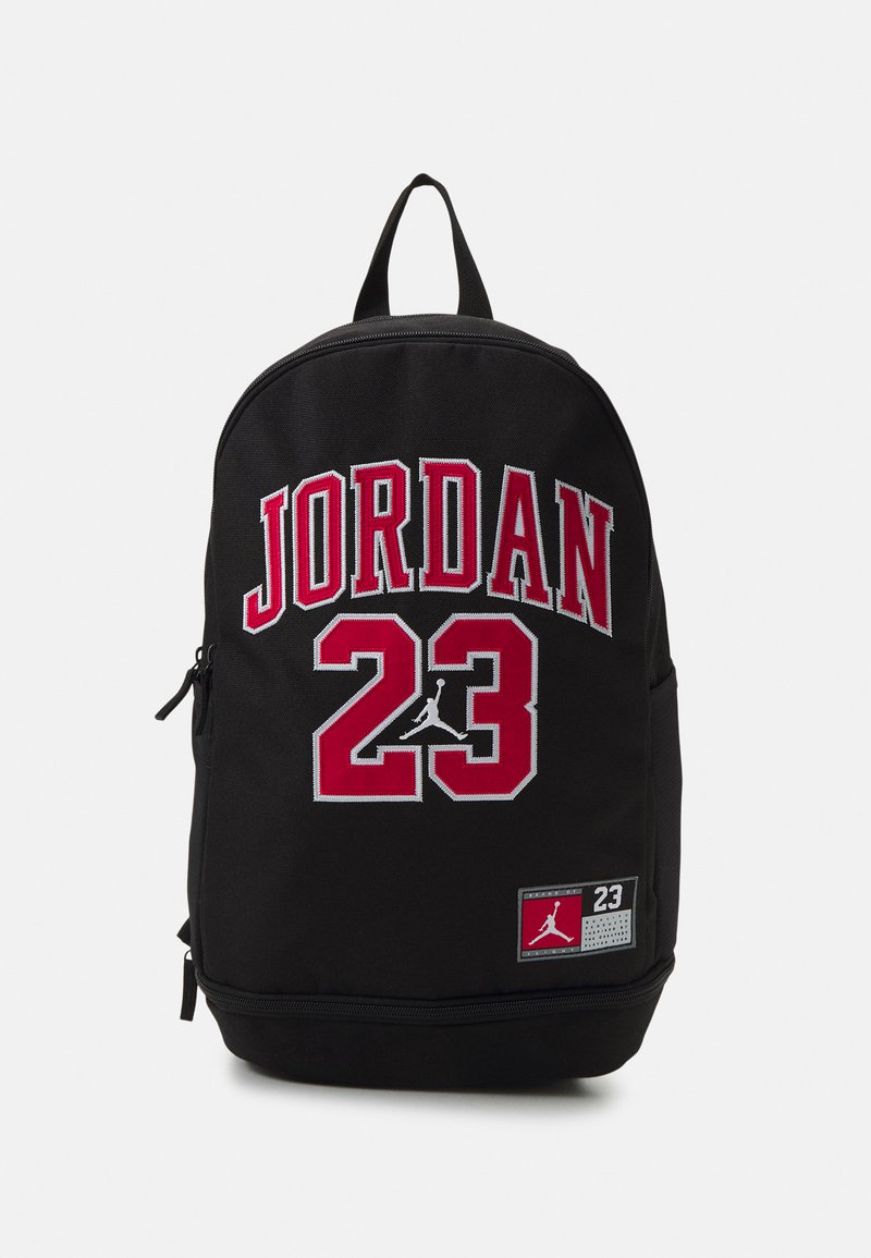 Zaino nero con ricami rossi "JORDAN" e "23". Presenta il logo Jordan sulla parte anteriore, una maniglia superiore e una tasca frontale con zip.