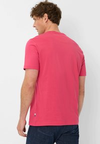 T-shirt in cotone rosa con maniche corte e collo rotondo, caratterizzata da un piccolo accento colorato all'orlo, indossata con jeans blu scuro.