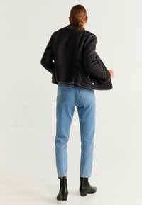 Schwarze cropped Jacke mit Shearling-Kragen, kombiniert mit hellblauen High-Waist-Jeans und schwarzen, kniehohen Stiefeln mit Absatz.