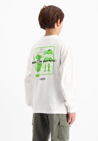 Weißes Langarm-T-Shirt mit großem grünen Grafikdesign auf der Rückseite, das verspielte Motive und den Text "BLCK BNNS" in fetter schwarzer Schrift enthält.