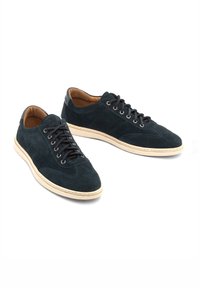 Sötétkék velúr sneaker, bézs gumi talppal, kerek orral és fűzős kialakítással. Kontrasztos varrás és sima bőr sarokdísz jellemzi.