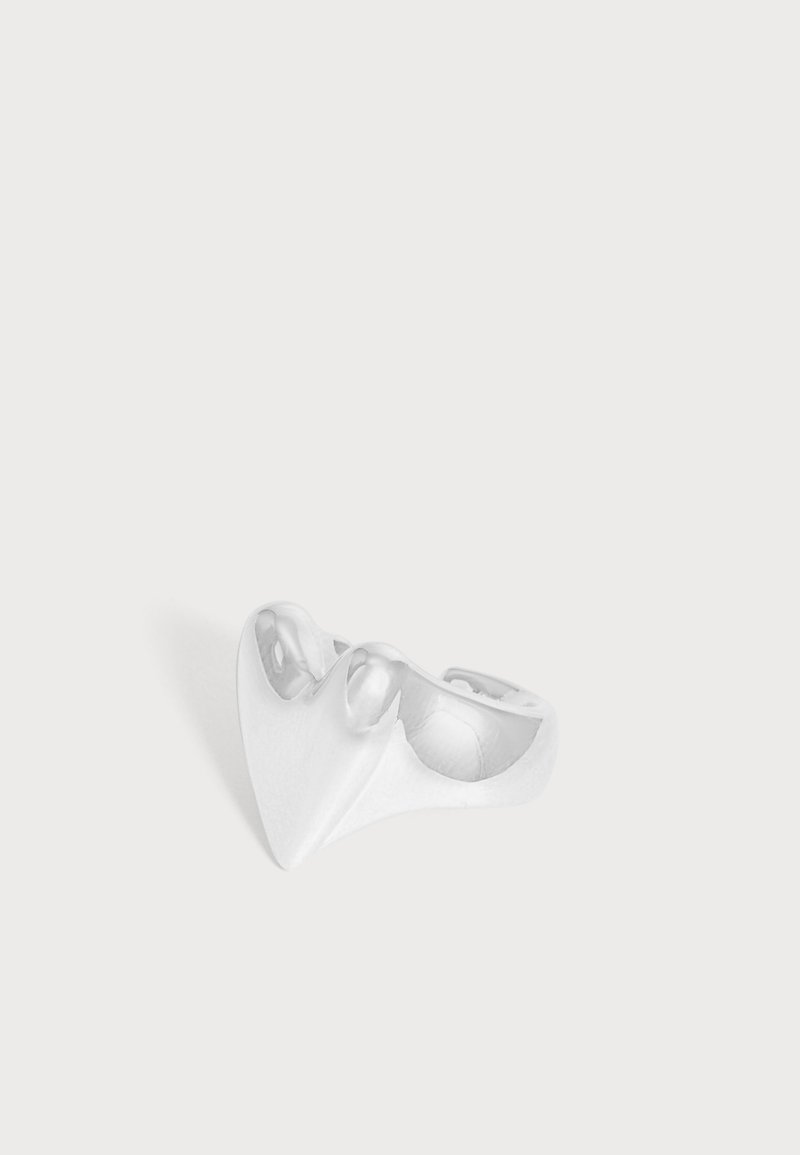 Un objet en céramique blanc et sculptural, aux formes courbes évoquant des bols, repose sur une surface claire.
