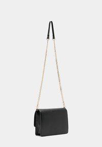 Černá kožená kabelka obdélníkového tvaru. Disponuje zlatým řetízkovým pop ruhem a elegantním designem, který ukazuje texturovaný povrch.