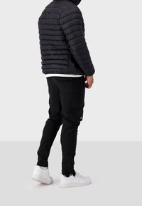 Giacca a vento nera con design a righe orizzontali, abbinata a pantaloni cargo neri. Le sneakers bianche completano l'outfit.