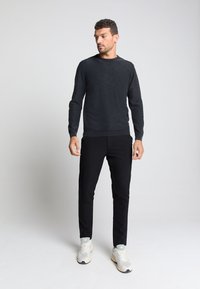 Zwarte gebreide trui met een ronde hals, lange mouwen, gecombineerd met zwarte tapered broek en lichtgekleurde sneakers. Eenvoudig en modern ontwerp.